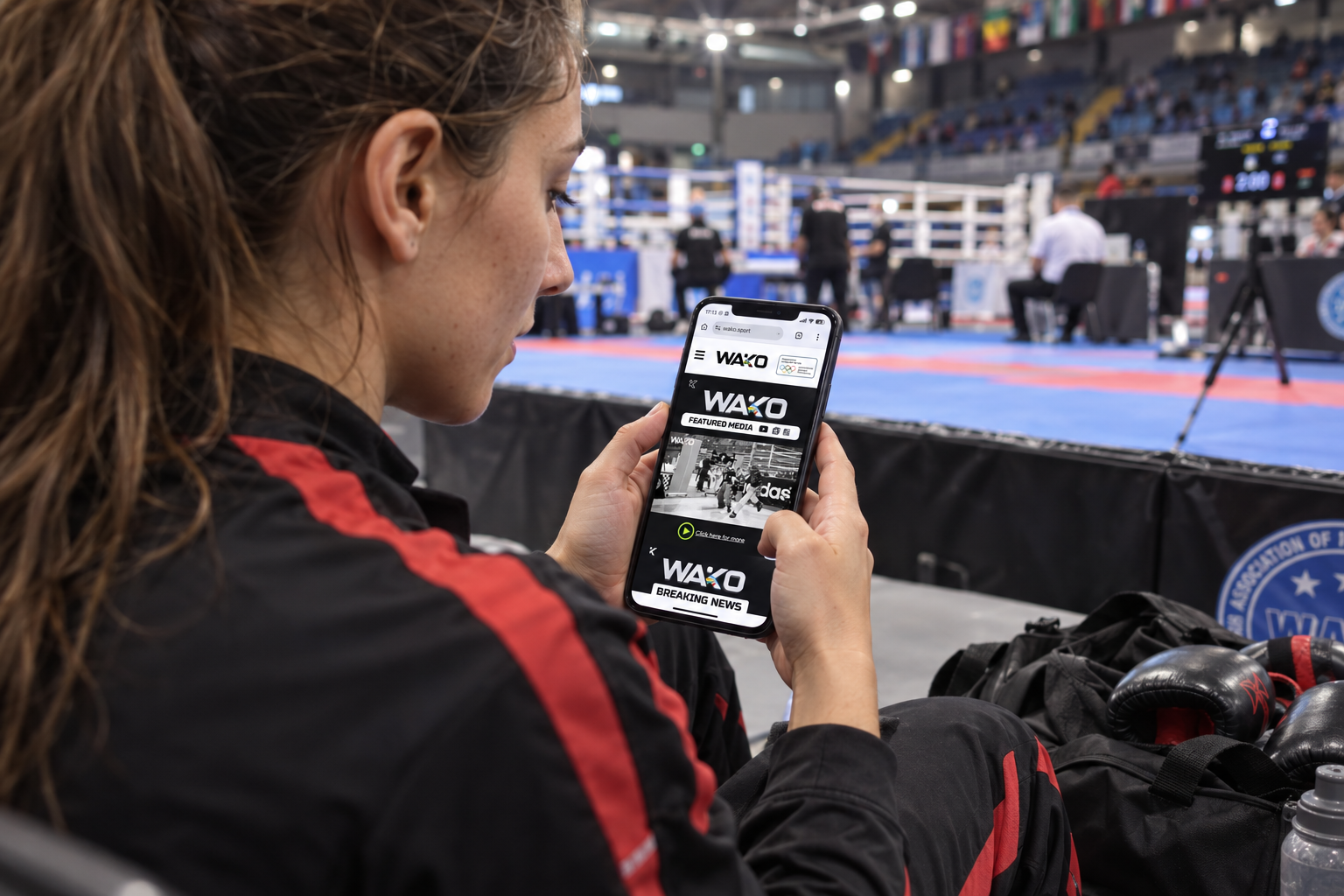 WAKO.sport viewed on a phone beside a kickboxing arena